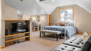 Un dormitorio con cama, televisor, ventilador de techo y ventana.
