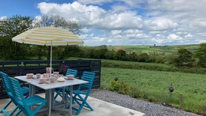 Un espace de restauration en plein air avec une table et des chaises, un parasol à rayures et une vue pittoresque sur un champ verdoyant et des collines.