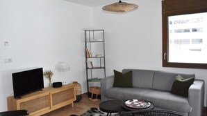 A modern living room with a grey sofa, a flat-screen TV, a wooden console, a woven pendant light, and a bookshelf.