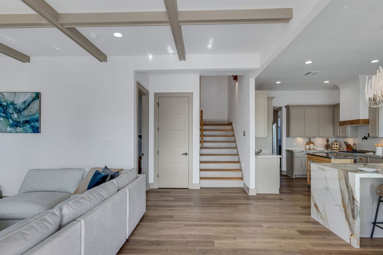 A modern interior with a staircase leading to a kitchen area, a living room with a sofa, and a dining area with a marble island.