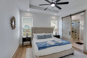 Une chambre à coucher avec un grand lit, un ventilateur de plafond, une porte-fenêtre coulissante et une table de chevet avec une lampe.