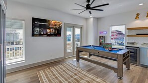 Un salon moderne équipé d’une table de billard, d’un ventilateur de plafond et d’un grand écran de télévision diffusant un match.