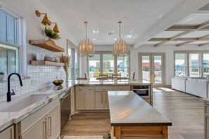 A modern kitchen with a large island, pendant lighting, and a view to the outside.