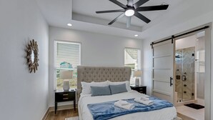 Une chambre avec un grand lit, un ventilateur de plafond, une porte-fenêtre coulissante et une table de chevet avec une lampe.