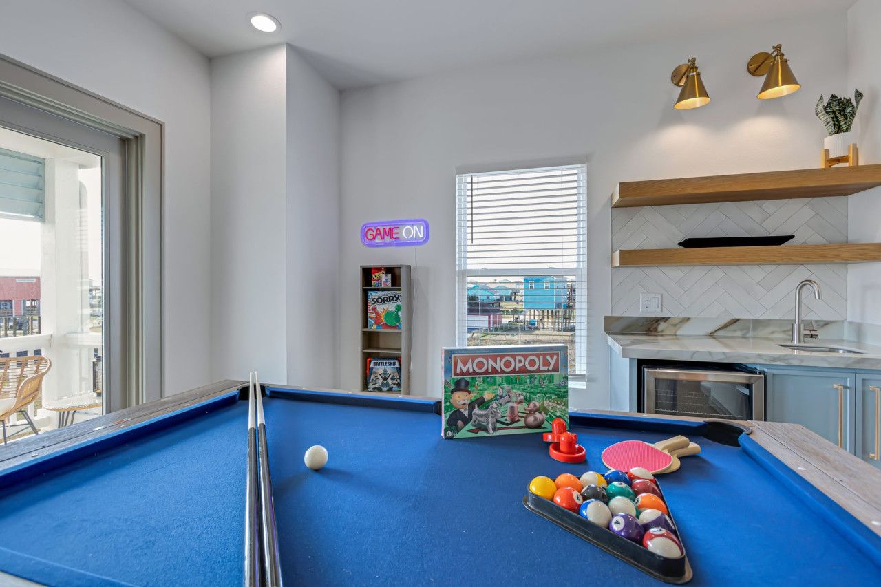 A pool table with a Monopoly board game, a neon sign, and a view of the outside.
