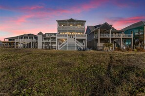 Une propriété située en bord de mer, comprenant plusieurs niveaux, des balcons et un escalier imposant menant à l’entrée.