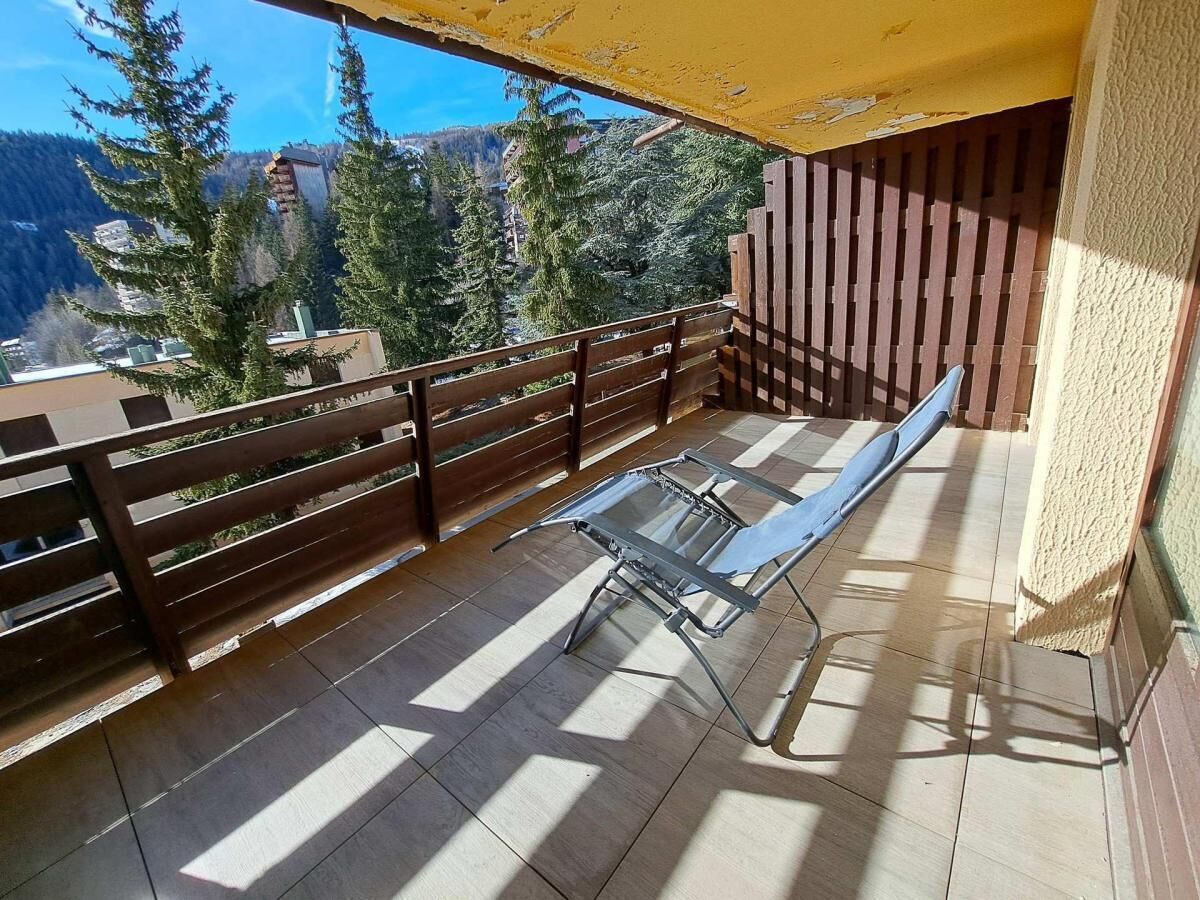 Un balcon avec une table en verre et des chaises en métal, des balustrades en bois et une vue sur les arbres et les bâtiments.