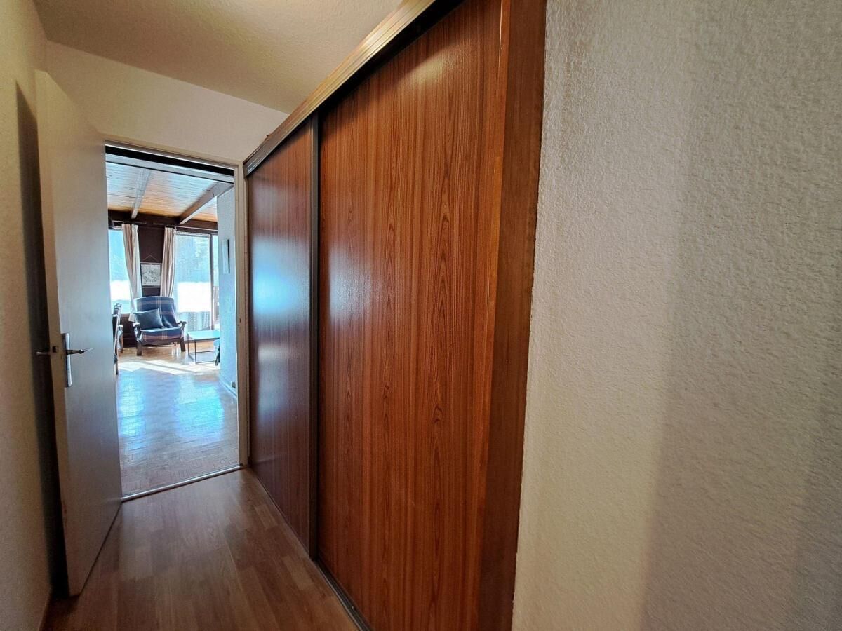 A hallway with a wooden door and a view into a room with a chair and a table.