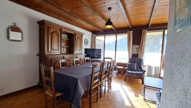 Et spiseområde med et træbord og stole, et fjernsyn og udsigt til det fri.