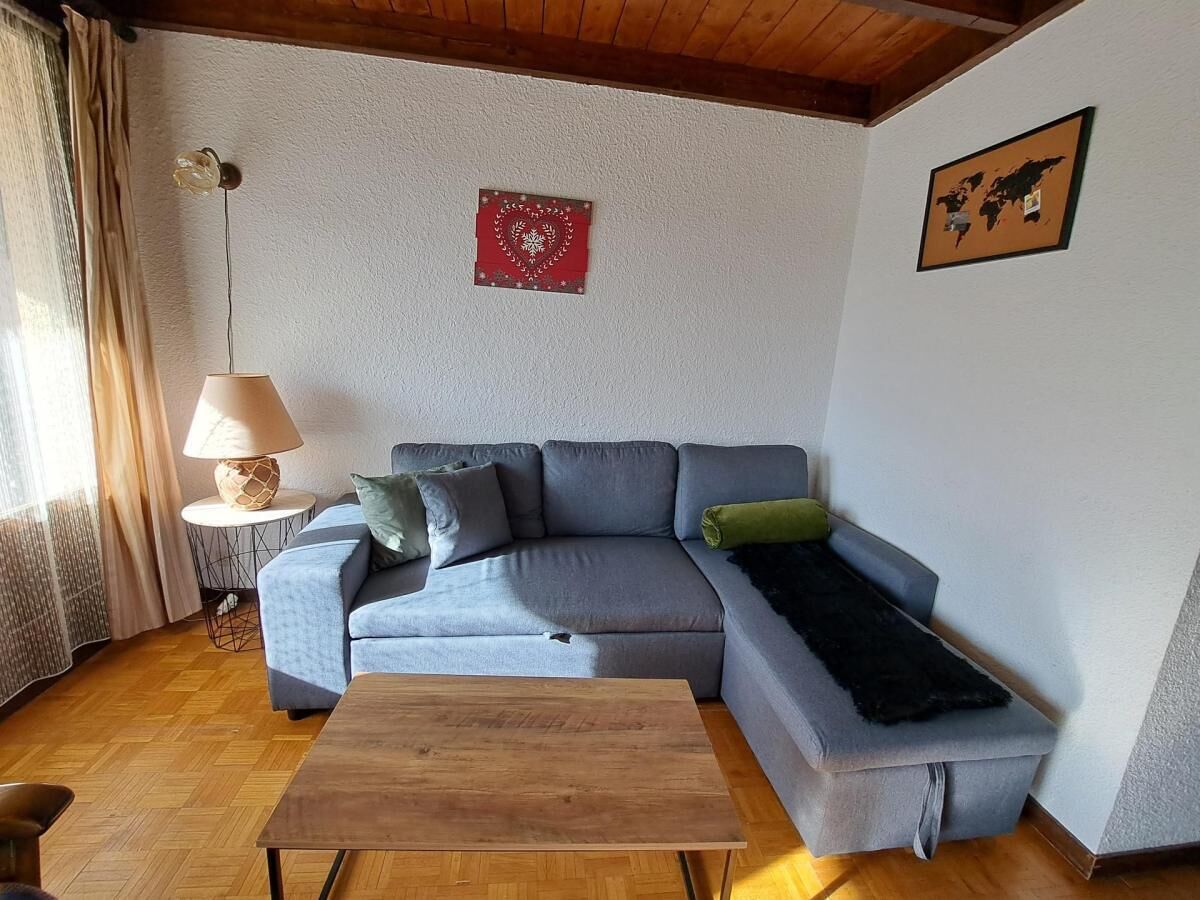 Uma sala de estar com um sofá cinza, uma mesa de centro de madeira, um abajur e uma decoração em formato de coração vermelho na parede.