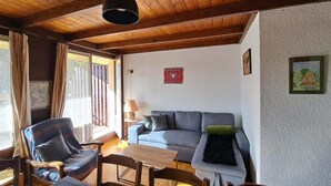 En hyggelig stue med træloft, sofa, lænestol, bord og lampe.