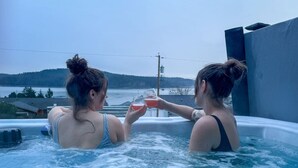 Deux personnes dans un jacuzzi, avec vue sur un lac et des collines en arrière-plan.
