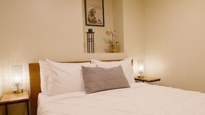 A neatly made bed with white linens and a single gray pillow, flanked by two bedside tables with lamps. - The Banksy-Greystone Rooftop Firepit United Center (Chicago)