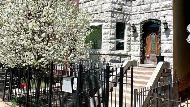 A stone building with a wooden door and windows, surrounded by a black metal fence. - The Banksy-Greystone Rooftop Firepit United Center (Chicago)