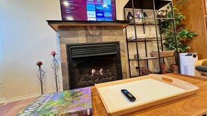 A living room with a fireplace, a flat-screen TV mounted above it, a book titled 'MONET A RETROSPECTIVE' on a table, and a remote control. - The Banksy-Greystone Rooftop Firepit United Center (Chicago)