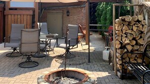 A patio area with outdoor seating, a fire pit, and a stack of firewood. - The Banksy-Greystone Rooftop Firepit United Center (Chicago)