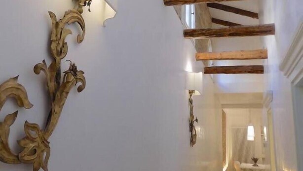 A hallway with exposed wooden beams, a wall-mounted light fixture, and a decorative metal piece. - LA Grande Bellezza (Venezia)