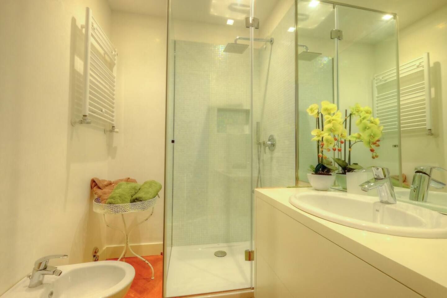 A modern bathroom with a glass shower enclosure, a white sink, and a mirror with a potted orchid.