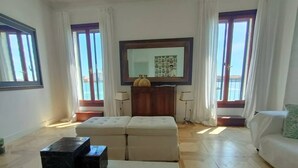 A spacious living room with a large flat-screen TV, a beige sofa, a white armchair, and a coffee table. - LA Grande Bellezza (Venezia)