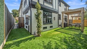Een modern herenhuis met een verzorgd gazon en een houten pergola met buitenmeubels.