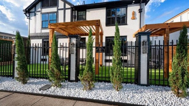 Een modern huis met twee verdiepingen, een witte gevel, zwarte accenten en een houten pergola in de voortuin.