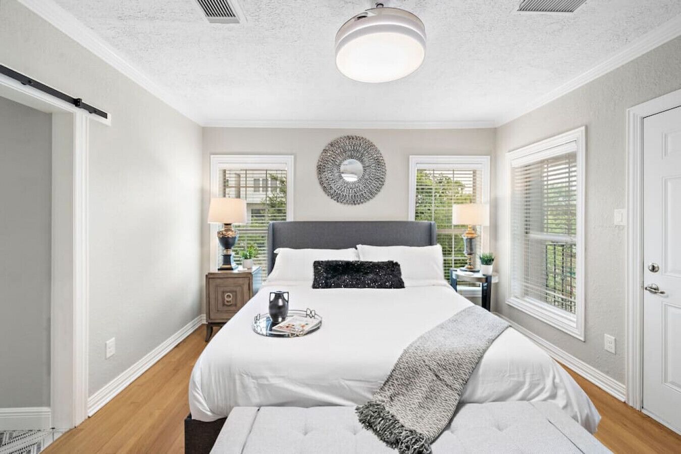 A bedroom with a large bed, bedside tables, a wall clock, and a window with blinds.