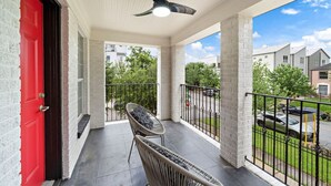 A balcony with a red door, a ceiling fan, and a view of neighboring buildings. - The Queen’s Gambit II (Houston)