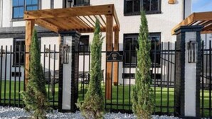 Une maison moderne à deux étages, dotée d’une pergola en bois, d’une entrée sécurisée par un portail et d’une pelouse bien entretenue.