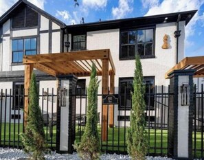 A modern two-story house with a wooden pergola, a gated entrance, and a well-maintained lawn. - The Bishop's Haven 2 (Houston)