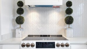Une cuisine avec un dosseret en carreaux de céramique blancs disposés en chevron, une hotte de cuisson centrale et deux plantes ornementales en pot.