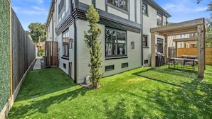 Une maison moderne à deux étages, dotée d’une pelouse bien entretenue et d’une pergola en bois avec un espace salon extérieur.