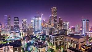 A cityscape at night with illuminated buildings and a construction crane. - The King's Retreat I (Houston)