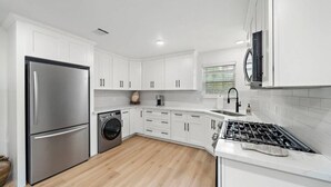 A modern kitchen with white cabinets, stainless steel appliances, and a wooden floor. - The King's Retreat I (Houston)