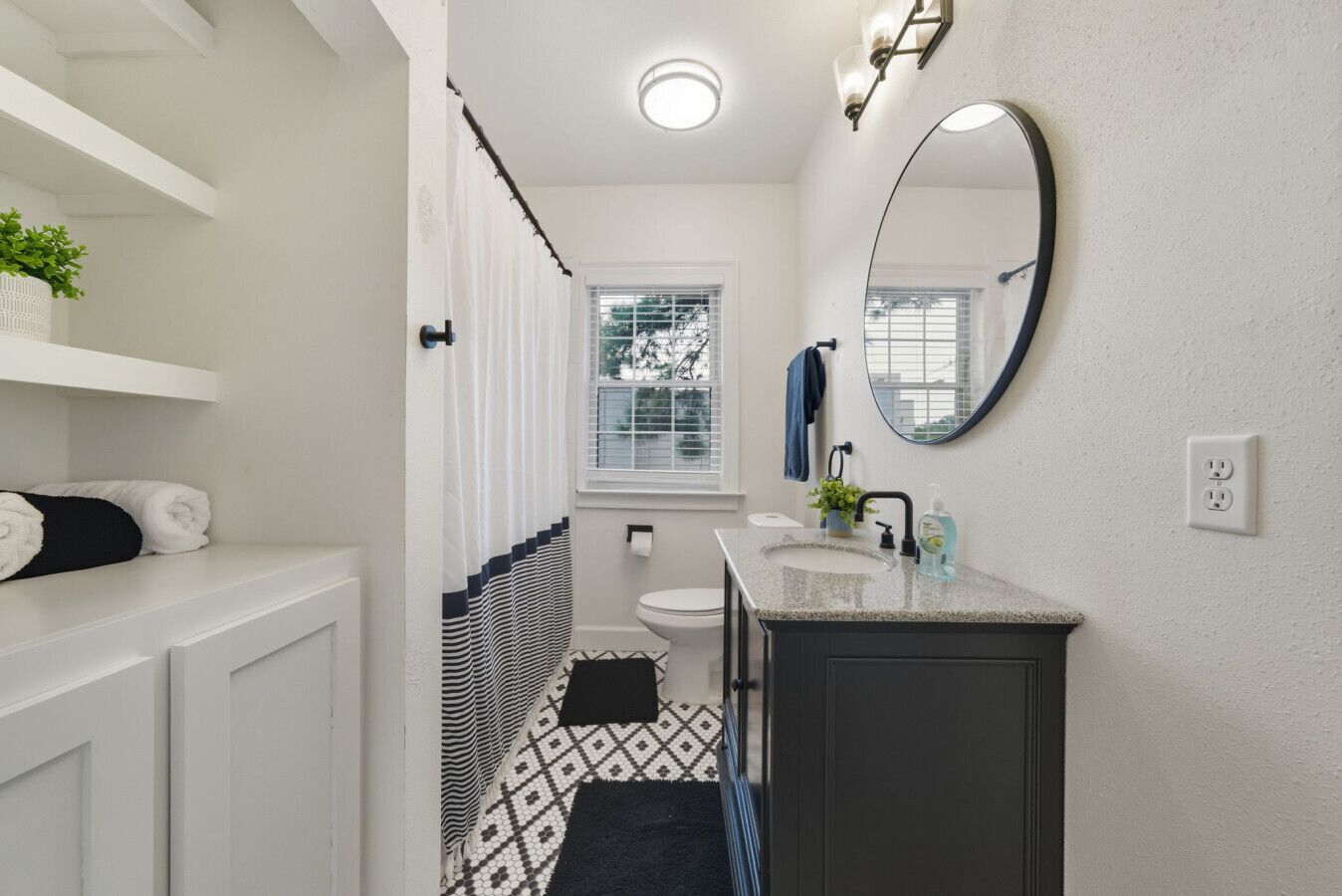 A bathroom with a white vanity, a round mirror, a window, and a towel rack.