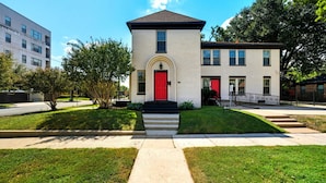 A two-story building with a red door, a small front porch, and a well-maintained lawn. - The King`s Castle II (Houston)