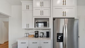 A kitchen with white cabinets, a stainless steel refrigerator, a microwave, and a coffee maker. - The King`s Castle II (Houston)