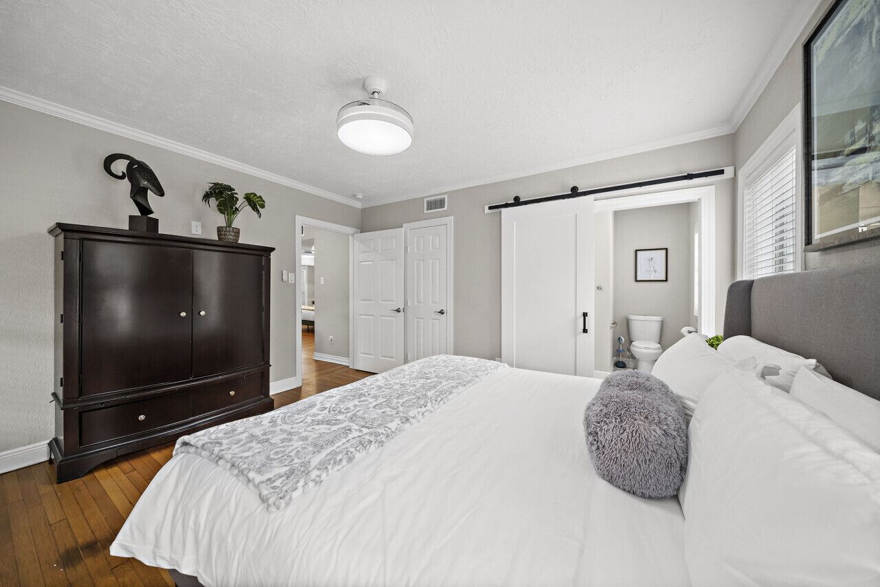 A bedroom with a bed, a dresser, a ceiling fan, and a door leading to another room.