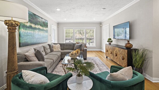 A spacious living room with a grey sectional sofa, green armchairs, a coffee table, and a large painting. - The Queen's Gambit I (Houston)