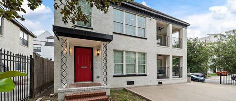 A two-story residential building with a red door, brick steps, and a small front porch.