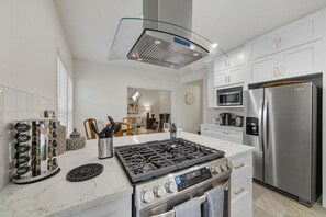 Une cuisine moderne avec des meubles blancs, un réfrigérateur en acier inoxydable, une cuisinière à gaz et une hotte en verre au-dessus de la plaque de cuisson.