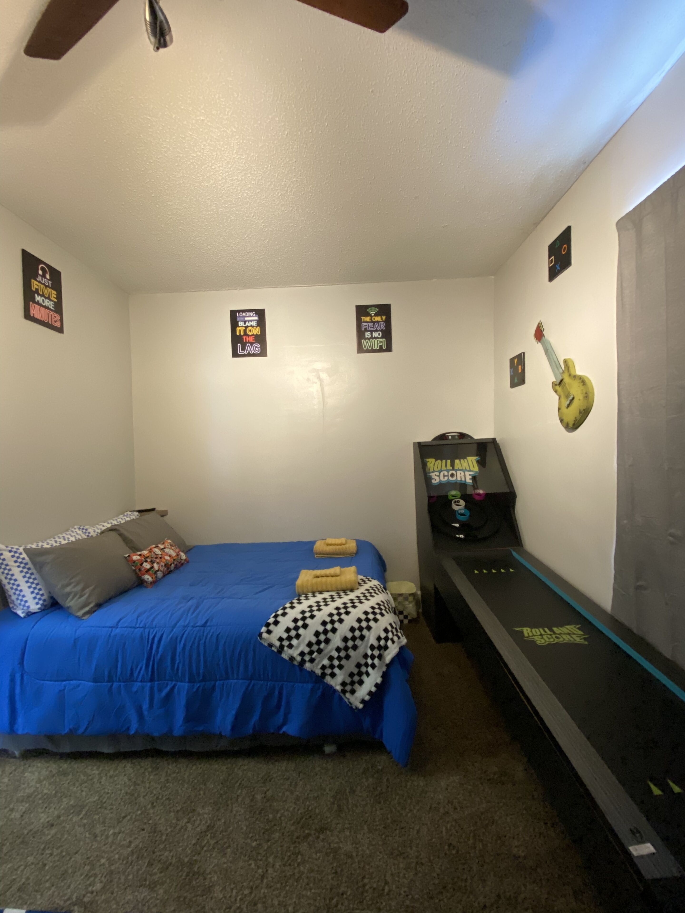 A bedroom with a bed, pillows, a wall-mounted guitar, and a treadmill.