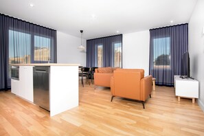 A modern living room with a kitchen area, wooden flooring, and large windows with curtains. - Les Lofts de Vitré - Par Les Lofts Vieux-Québec (Québec City)