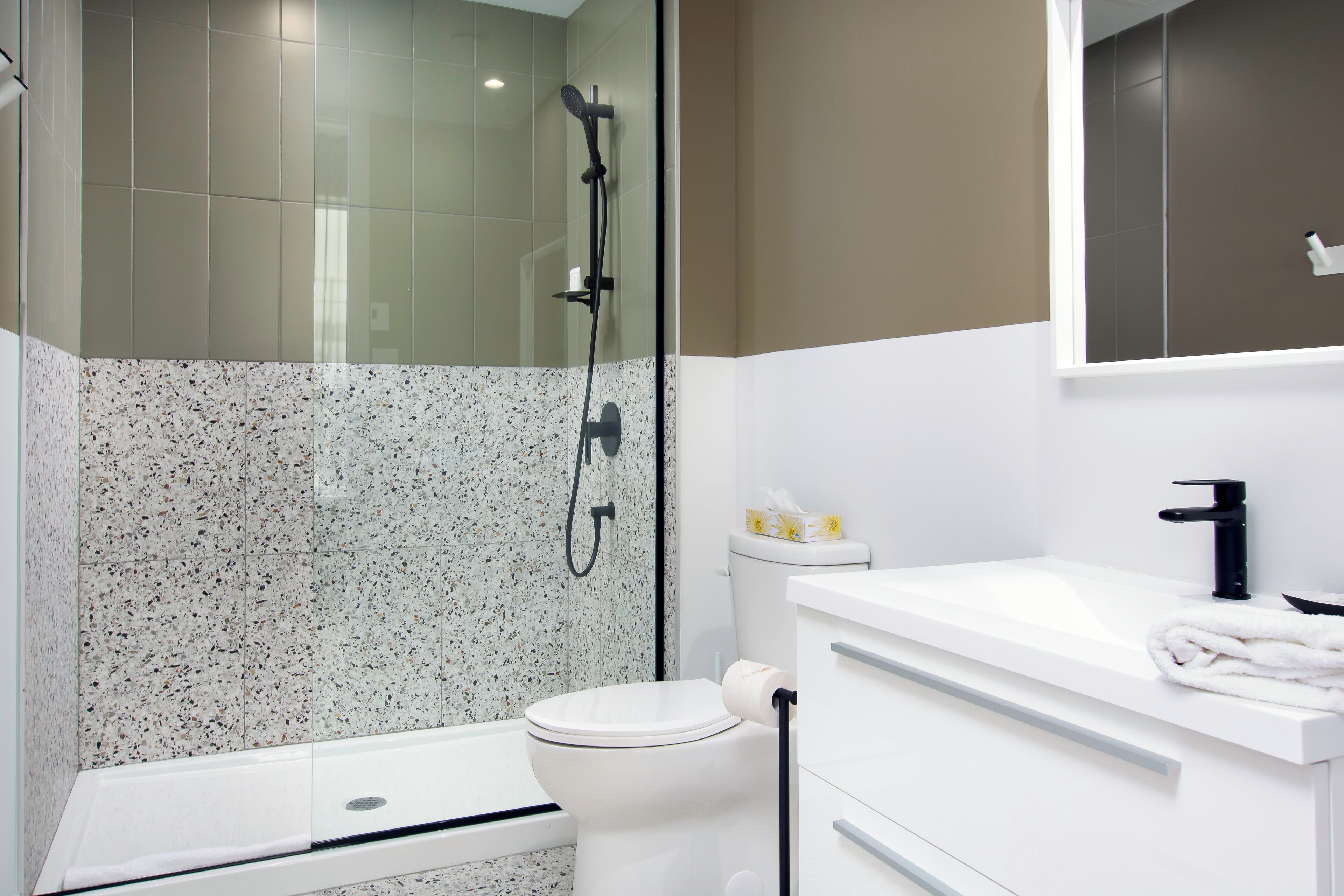 Un baño moderno con ducha envuelta en vidrio, inodoro blanco y lavamanos blanco con una toalla.