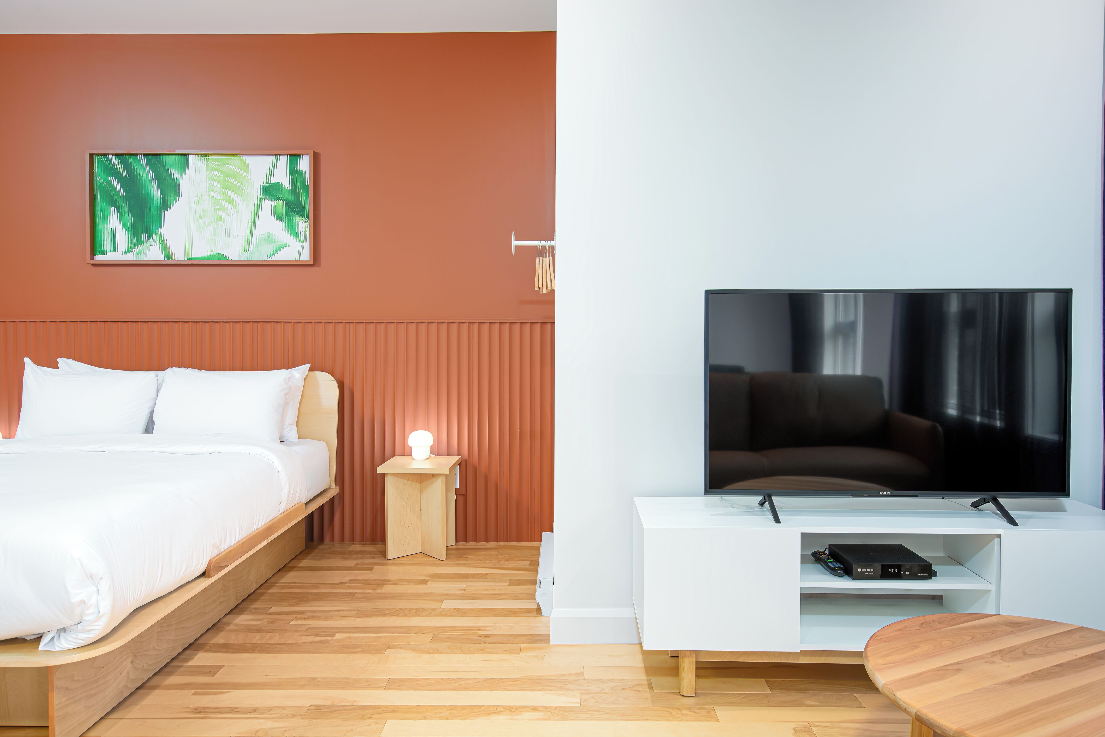 A modern hotel room with a bed, a TV, a small table, and a wall-mounted artwork.