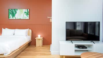 A modern hotel room with a bed, a TV, a small table, and a wall-mounted artwork.