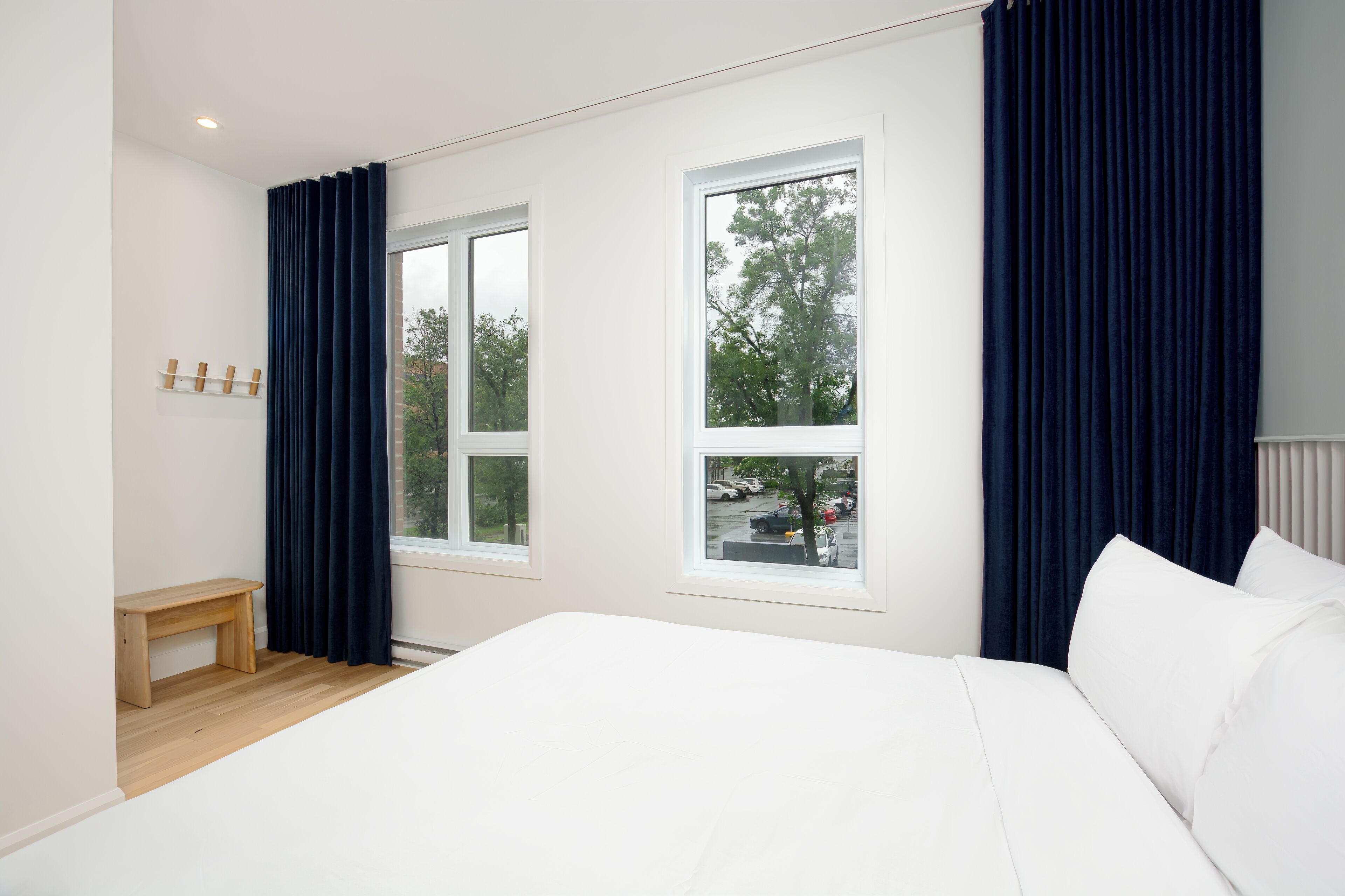 A bedroom with a large bed, two windows, a bench, and a coat rack.