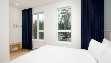 A bedroom with a large bed, two windows, a bench, and a coat rack.