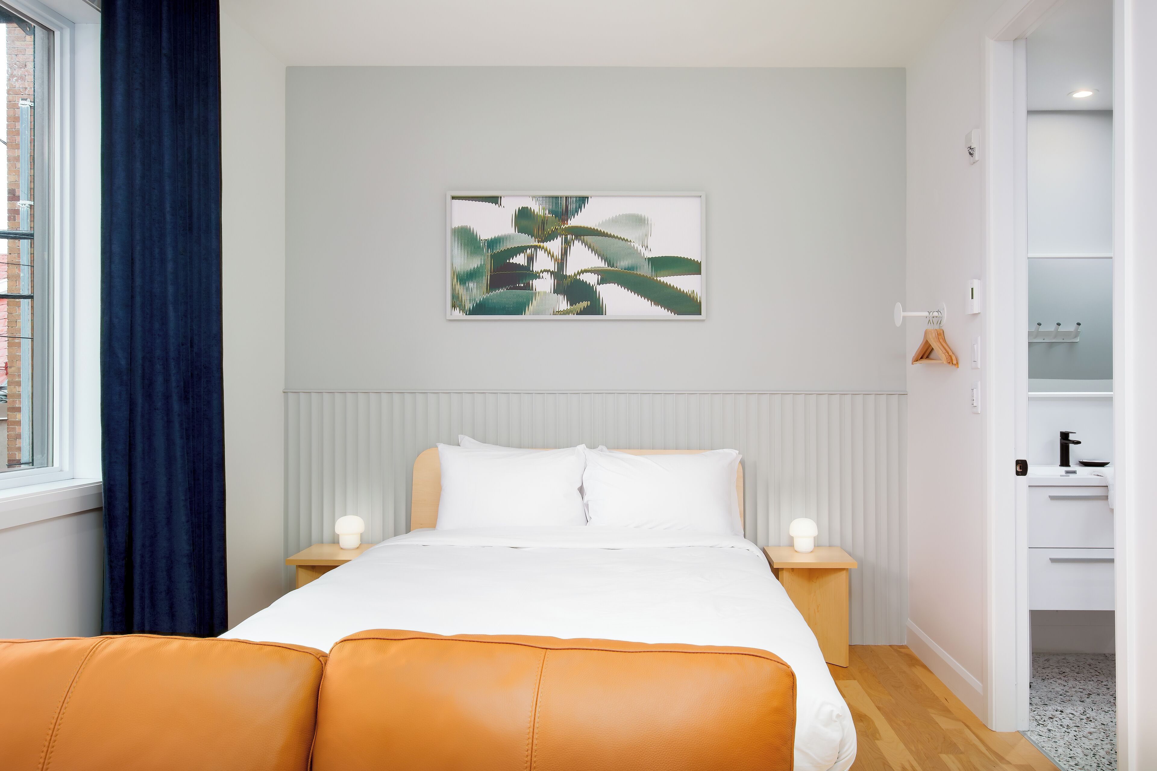 Un dormitorio con cama, mesita de noche, cómoda, ventana con cortinas y una obra de arte colgada en la pared.