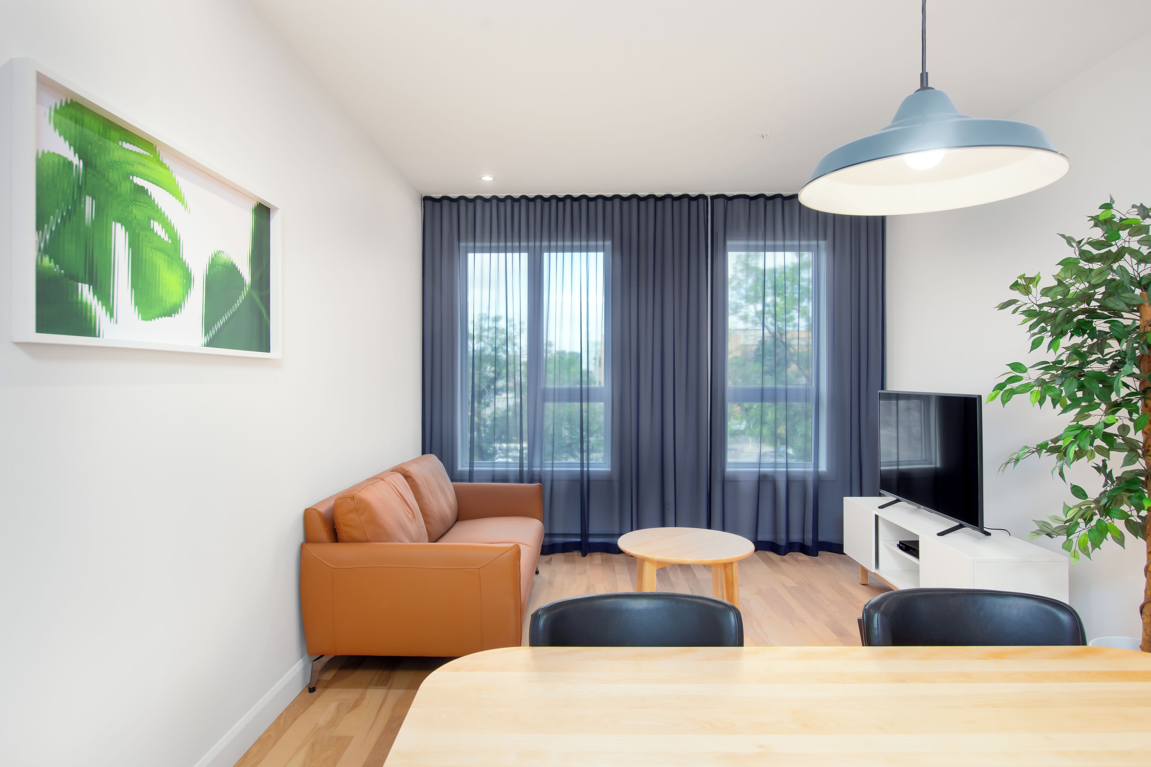 Un salon moderne comprenant un canapé, une table à manger, un téléviseur et une grande fenêtre agrémentée de rideaux.
