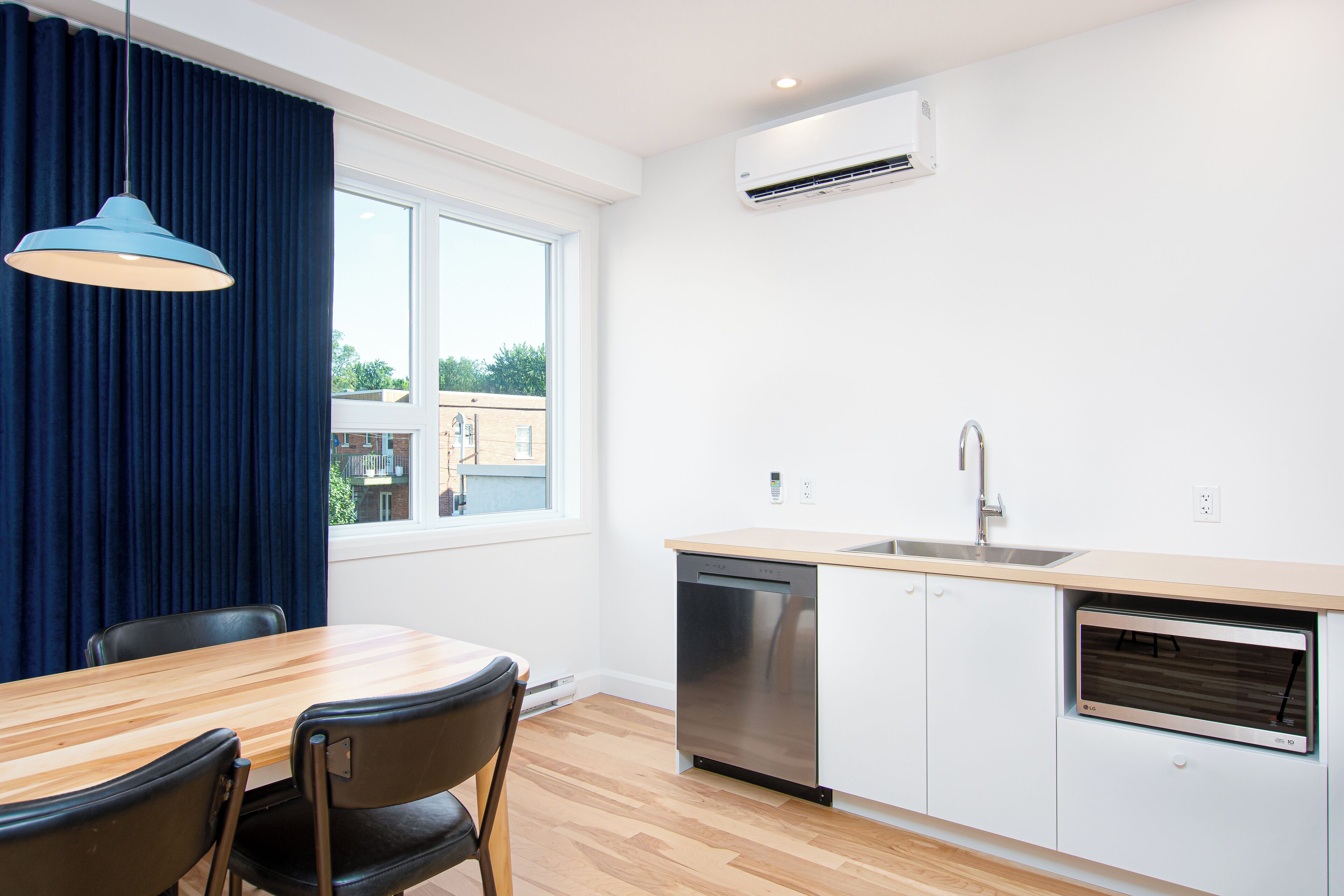 A modern kitchen with a dishwasher, sink, and window overlooking a building.